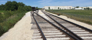 Two sets of railroad tracks going through a field towards a building in the distance.