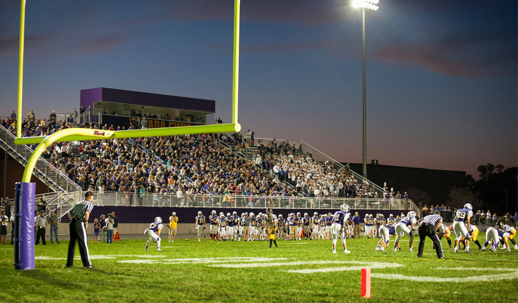 Football game at night, on the field behind goal post.