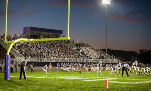 Football game at night, on the field behind goal post.