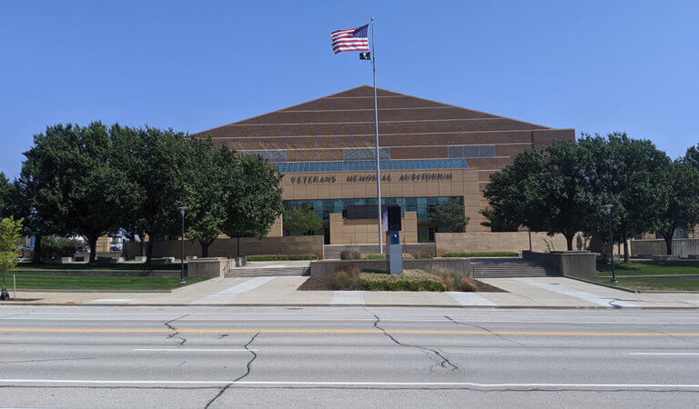 front of large auditorium with American flag flying