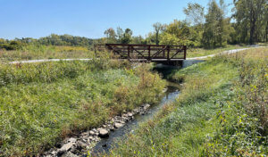 Wanatee bridge sits over a stream of water surrounded by native plantings