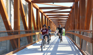 Family smiling as they ride across a trail bridge on bikes