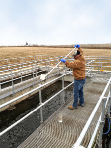 Water operator collecting sample from treatment plant pond