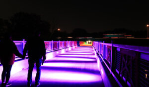 Couple walks across a lit up trail bridge at night