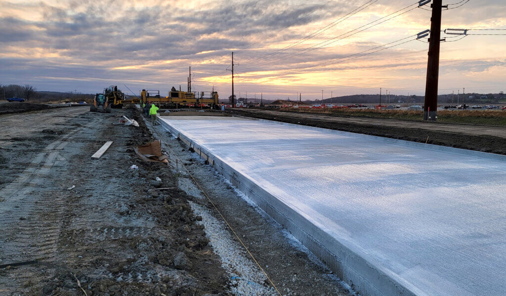 Newly poured roadway with road crew working in the background.