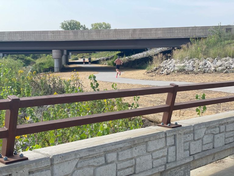 A man running on trail underneath bridge|Creek bank underneath bridge|Map of the new Clear Creek Trail alignment around the Interstate 80/380 interchange|Workers install one of the bridges over Clear Creek|Decorative Concrete castings for Clear Creek Trail Connection|Clear Creek Trail connection bridge|Trail underneath bridge in Coralville Iowa