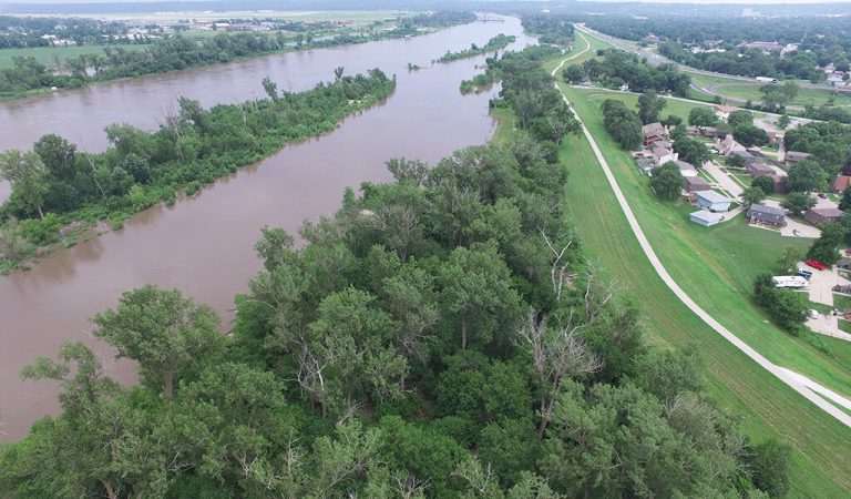 Aerial view of flooded river|floodwaters along walking trail|construction worker installing pipe|construction workers standing on levee||construction in council bluffs for levee reconstruction