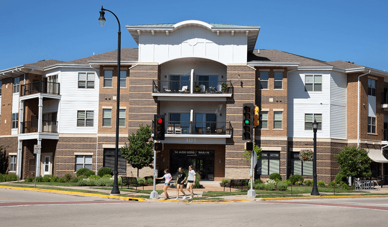 balconies of apartment building||woman walking dog past apartment building||business storefronts|greenery and flowers lining sidewalk