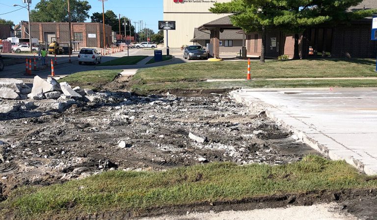 shattered concrete at an intersection|large gate valve exposed underground|sewer intake pipe sticking out of the ground|||new asphalt laid on a street