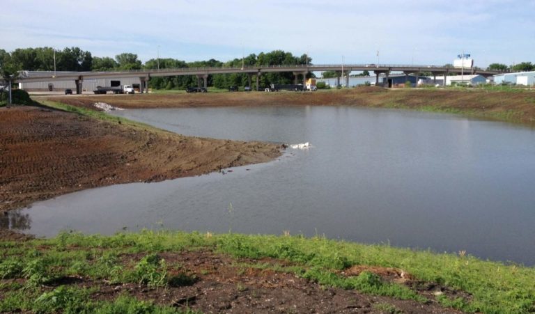 view of filled drainage basin|freshly poured concrete protected by traffic cones along a roadway|construction machines digging large hole for drainage basin|stormwater outlet|stormwater inlet structure|Our experts were tasked with developing stormwater improvements to mitigate common flooding.|street flooding leads to stormsewer and roadway improvements for Fort Dodge