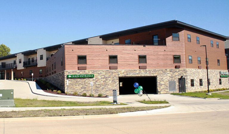 Senior living facilities||large red crane arching over construction site|construction workers adding cement flooring|digital rendering of commons crossing design|Large red crane over construction site and new building|Construction site|Senior living facilities|Senior living facilities