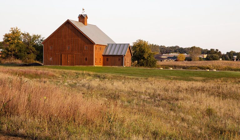 Large wood barn in grassy area|||single family homes in a neighborhood|grassy area with housing development in the background||large wood barn