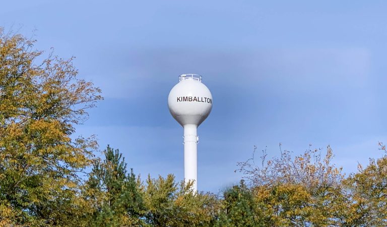 kimballton water tower above trees in blue sky|Large machine digging trench for blue water pipe.|Kimballtons new water next to shorter