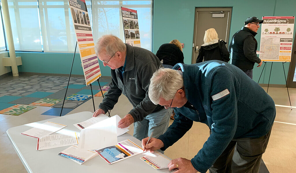 two men signing papers at an open house|aerial map view of indianola pavement pci summary|signaled intersection partially closed while construction is completed|snyder & associates planner answers questions about indianola comprehensive plan to citizen|construction crew finishing pavement