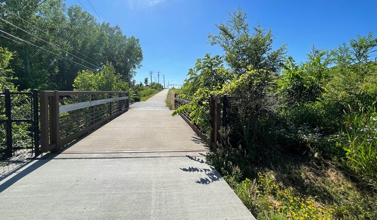 metal bridge crossing stream for bike and pedestrian trail||||||biker riding on trail off of high traffic roadway|Group of bikers ride on trail next to busy roadway|man riding on bike trail|man riding on bike trail at street crossing