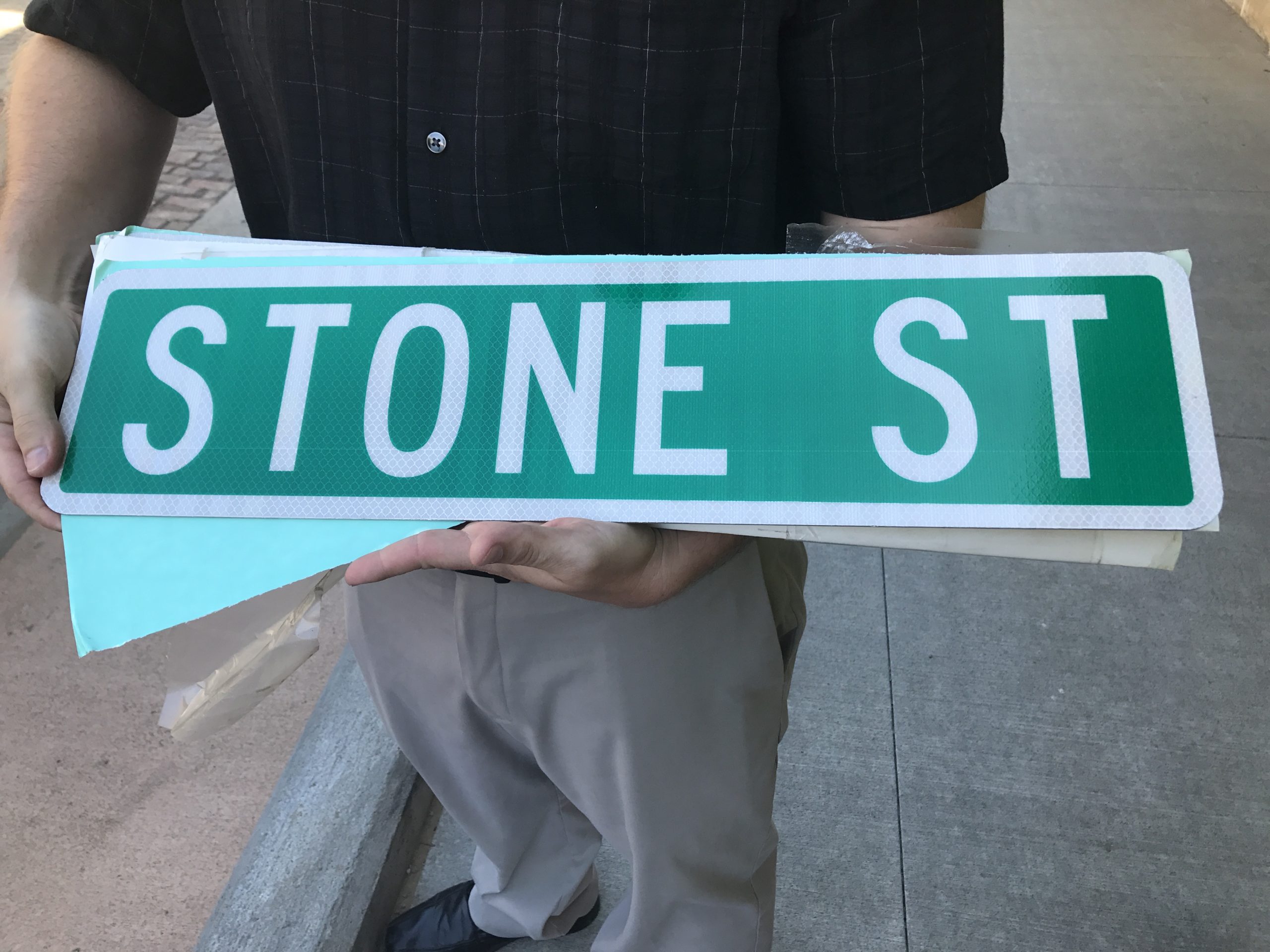 Close up of an unmounted street sign being held in the palm of a man. 