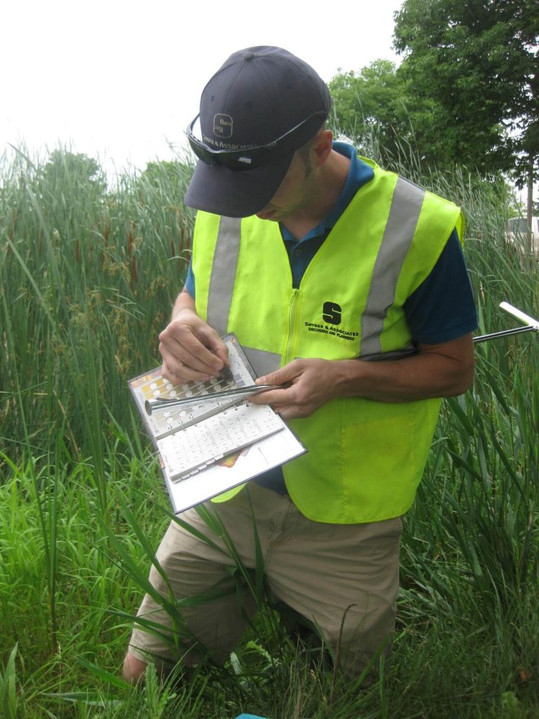 Snyder field employe wearing bright yellow vest testing soils for 404 permitting