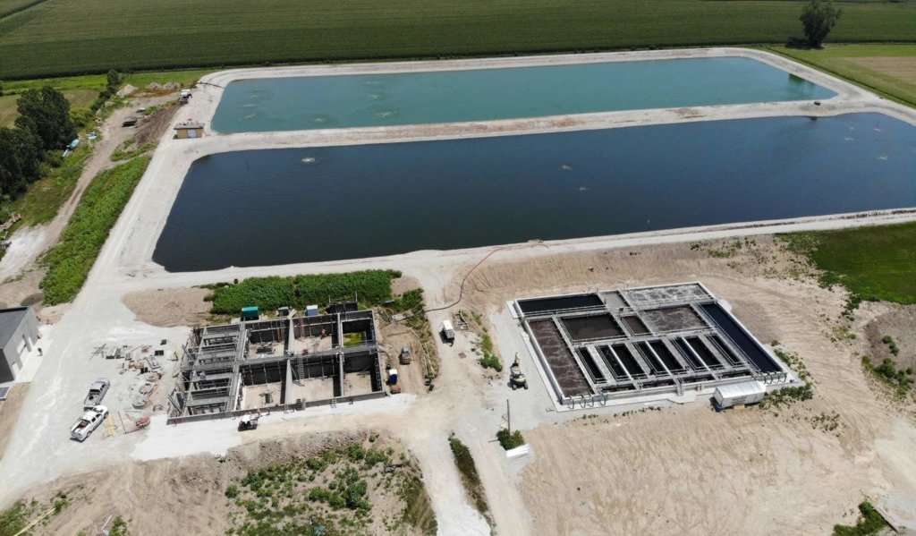 aerial view of two large blue lagoons and operation buildings||waterside view of lagoon and gravel shores|metal walkway between two lagoons. One is rough and one is smooth.||