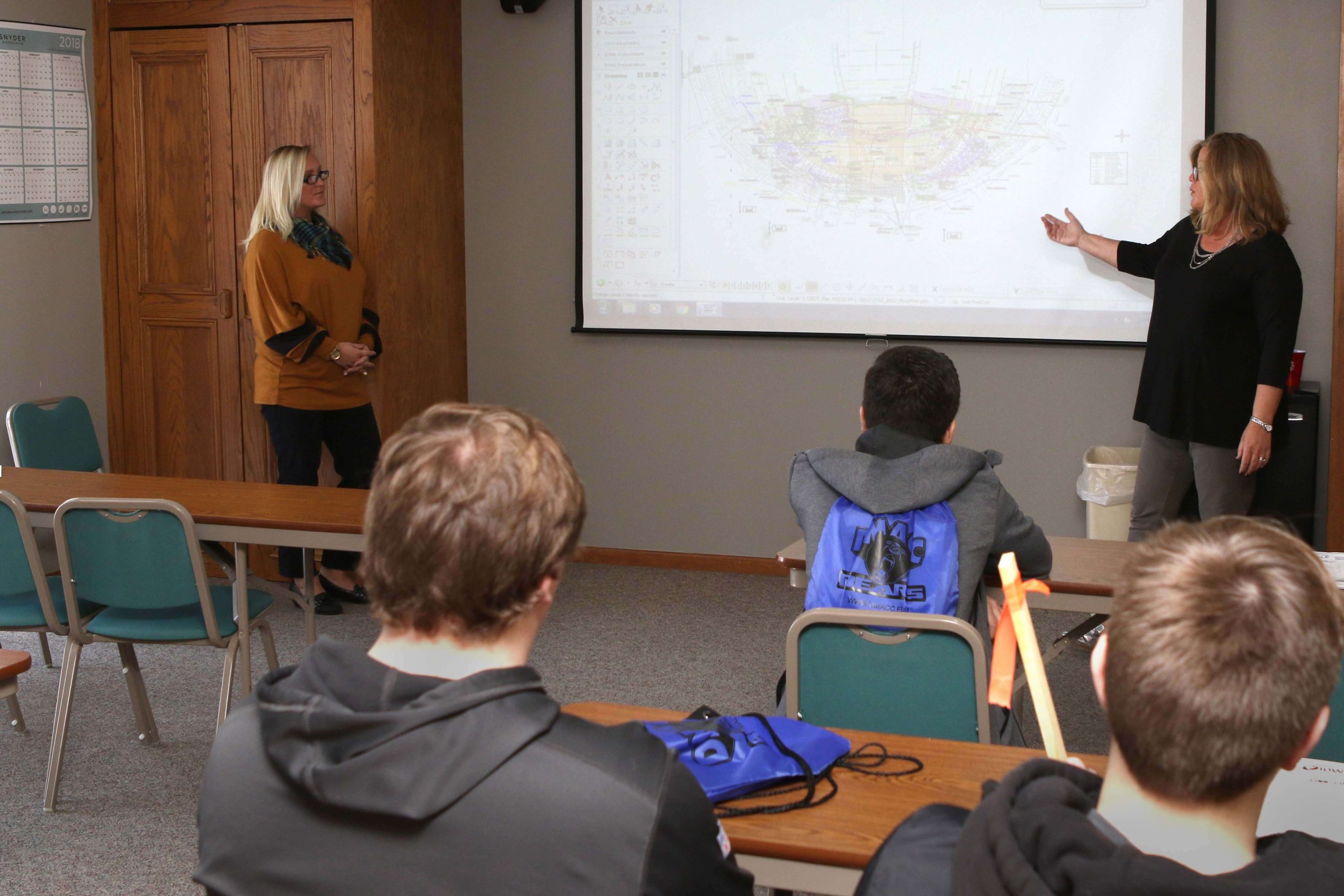 two women engineers stand in front of class and present