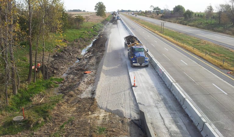 construction of extended roadway shoulders and drainage ditches|new metal guardrails placed along interstate||semi-truck driving on a new roadway