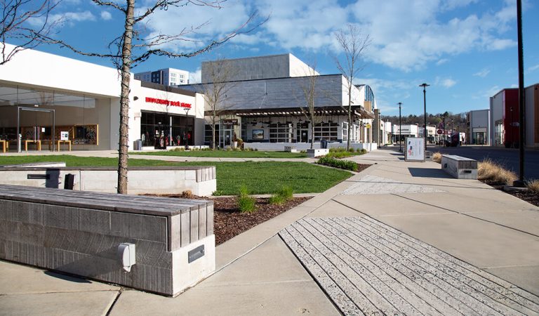 open courtyard at mall|lady walking dog through mall open space|landscaping outside of amc theatre|wide sidewalks leading up to bookstore|entry to macys