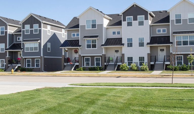 grey and white townhomes in a row||Brick apartment building and large brick sign that says The Bricks|New roadway||Rows of townhomes with vast greenspace||Businesses in a row and expansive parking