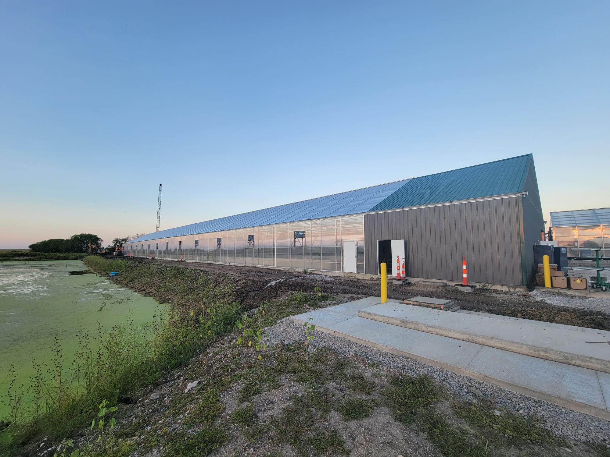 Slater wastewater treatment greenhouse at sunset|Wastewater lagoon with aeration bubbles|Greenhouse and settling pond|Aerial view of large lagoon cell drained for construction|Slater's new greenhouse for wastewater treatment|Inside Slater greenhouse with empty cells|Inside of slater wastewater treatment plant with algae belts.|Slater wastewater treatment plant ribbon cutting|visitors walk inside the new Slater greenhouse and view RAB belts|aerated lagoon at the slater wastewater treatment plant|RAB belts at the Slater wastewater treatment plant