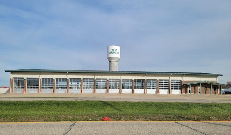 water tower behind public works building|concrete water tower base being constructed|West Burlington storage tank with small hole|workers buildig the tower base|painted water tower top being raised into place