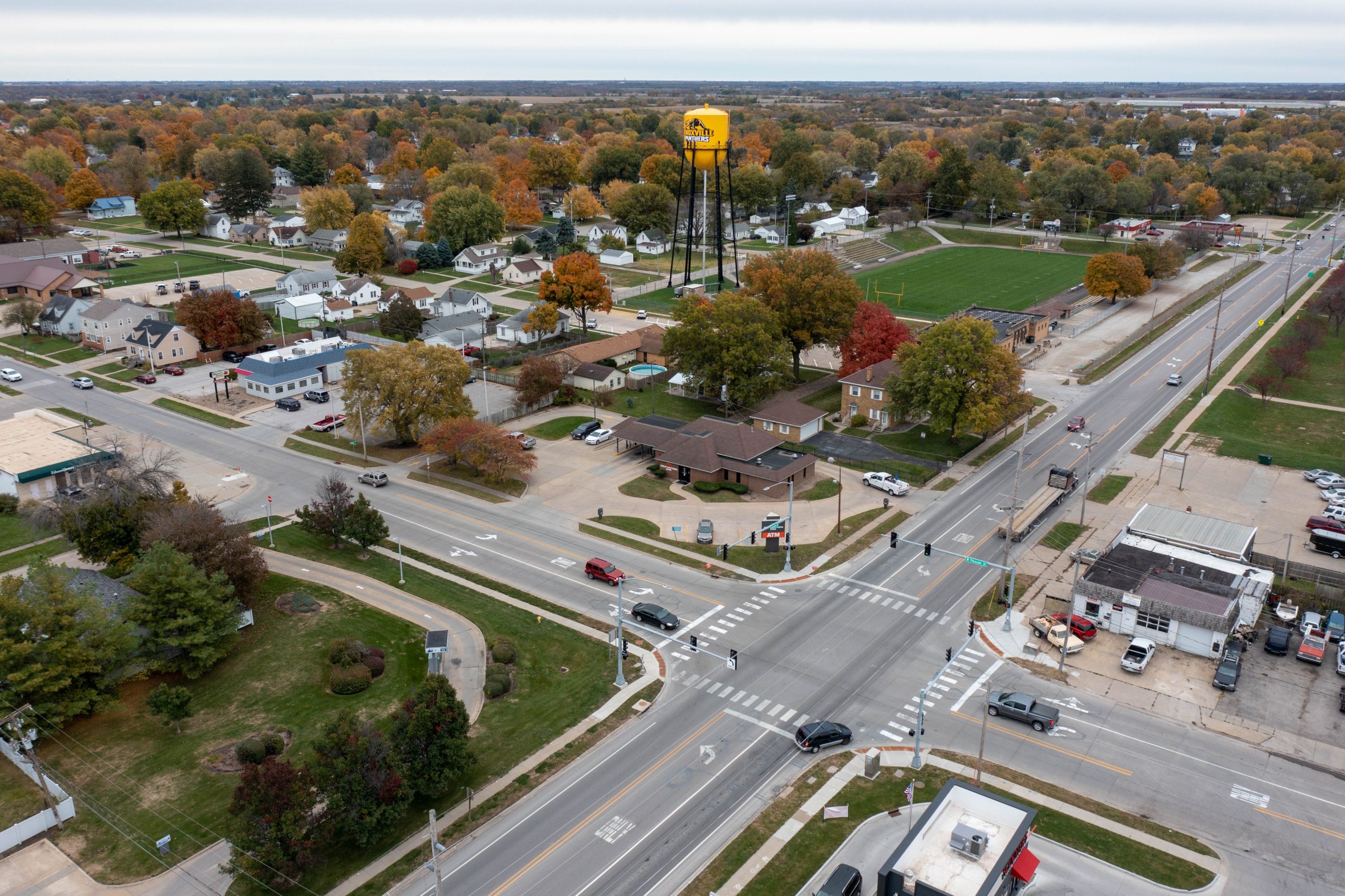 Aerial view of a grid of streets in a small town, with fall foliage and a yellow water tower at center.