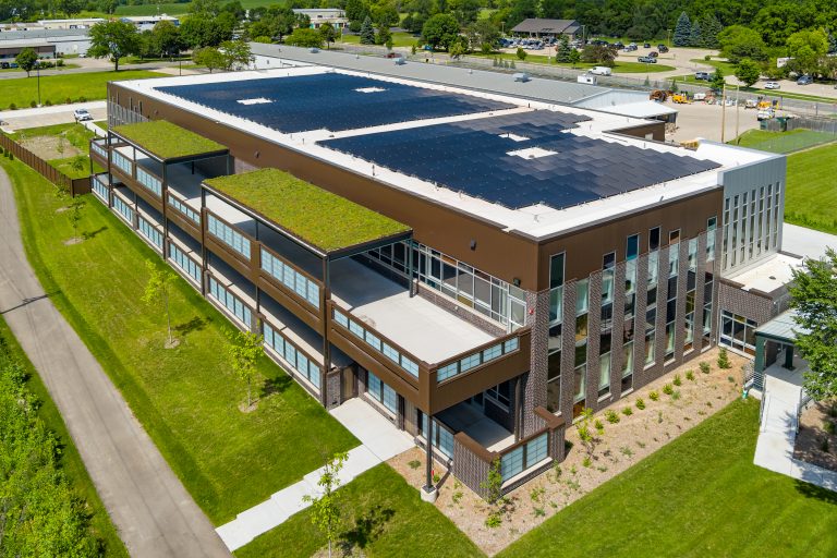 Aerial view of a modern brown brick building with extensive solar panels on the flat roof and green roof terraces.