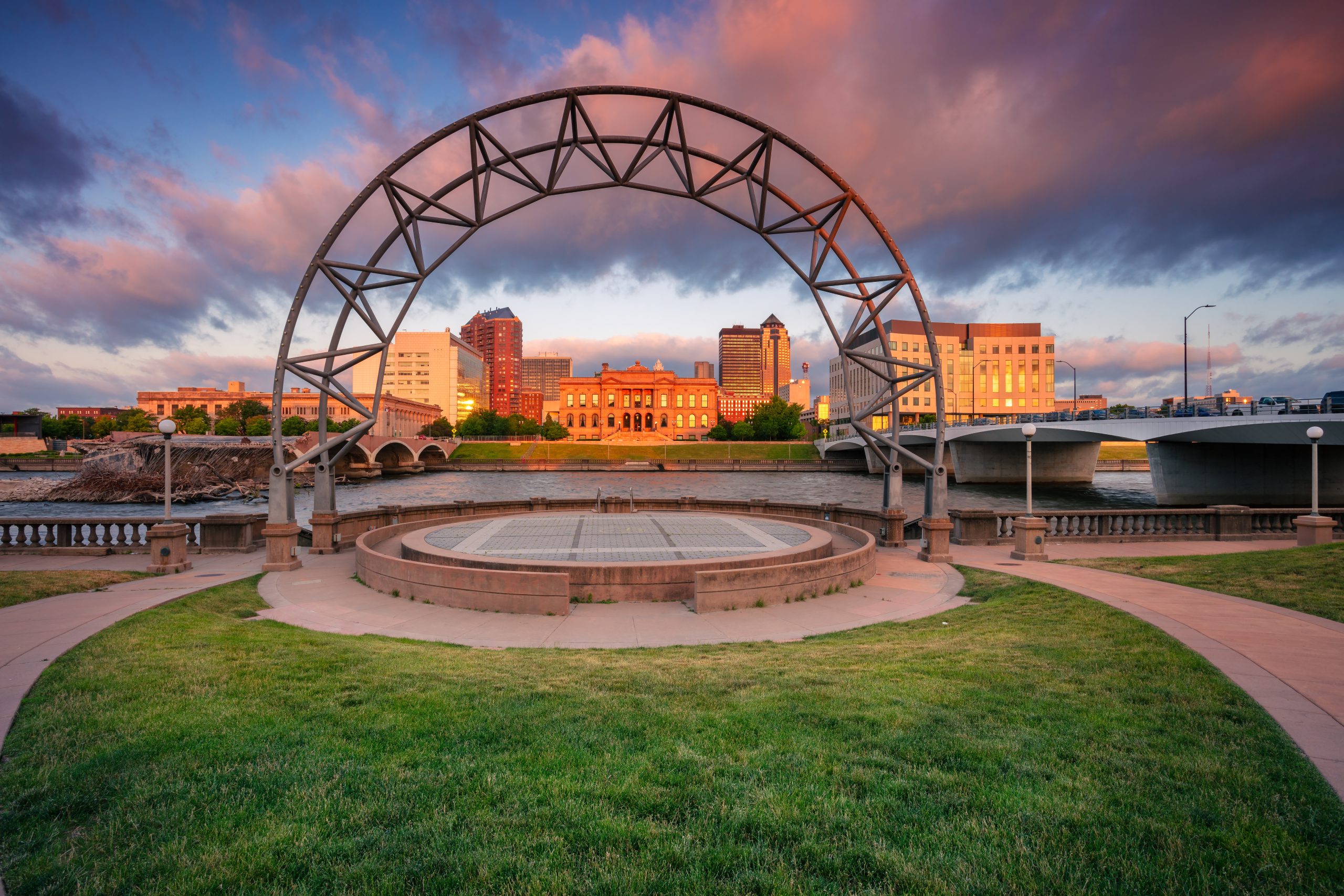 Des Moines, Iowa, USA. Cityscape image of Des Moines skyline, Iowa, USA at summer sunrise. Close-up of a woman with long, wavy blonde hair smiling outdoors, with a blurred natural background.